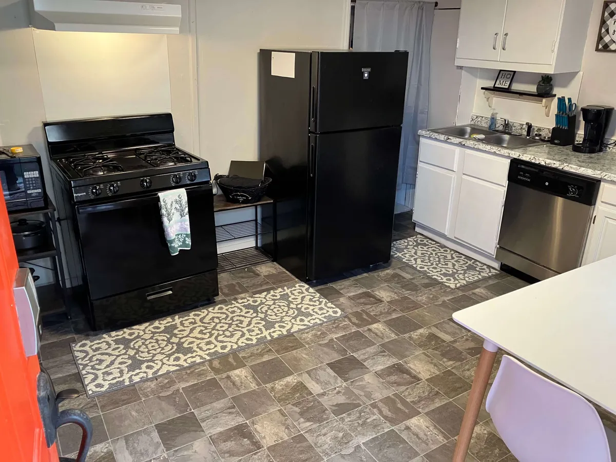 A comfortable and practical kitchenette highlighted by a black stove, black refrigerator, white cabinetry, a decorative rug, and visible countertop appliances including a coffee maker. The arrangement maximizes usability and reflects an efficient layout ideal for guests on the go.