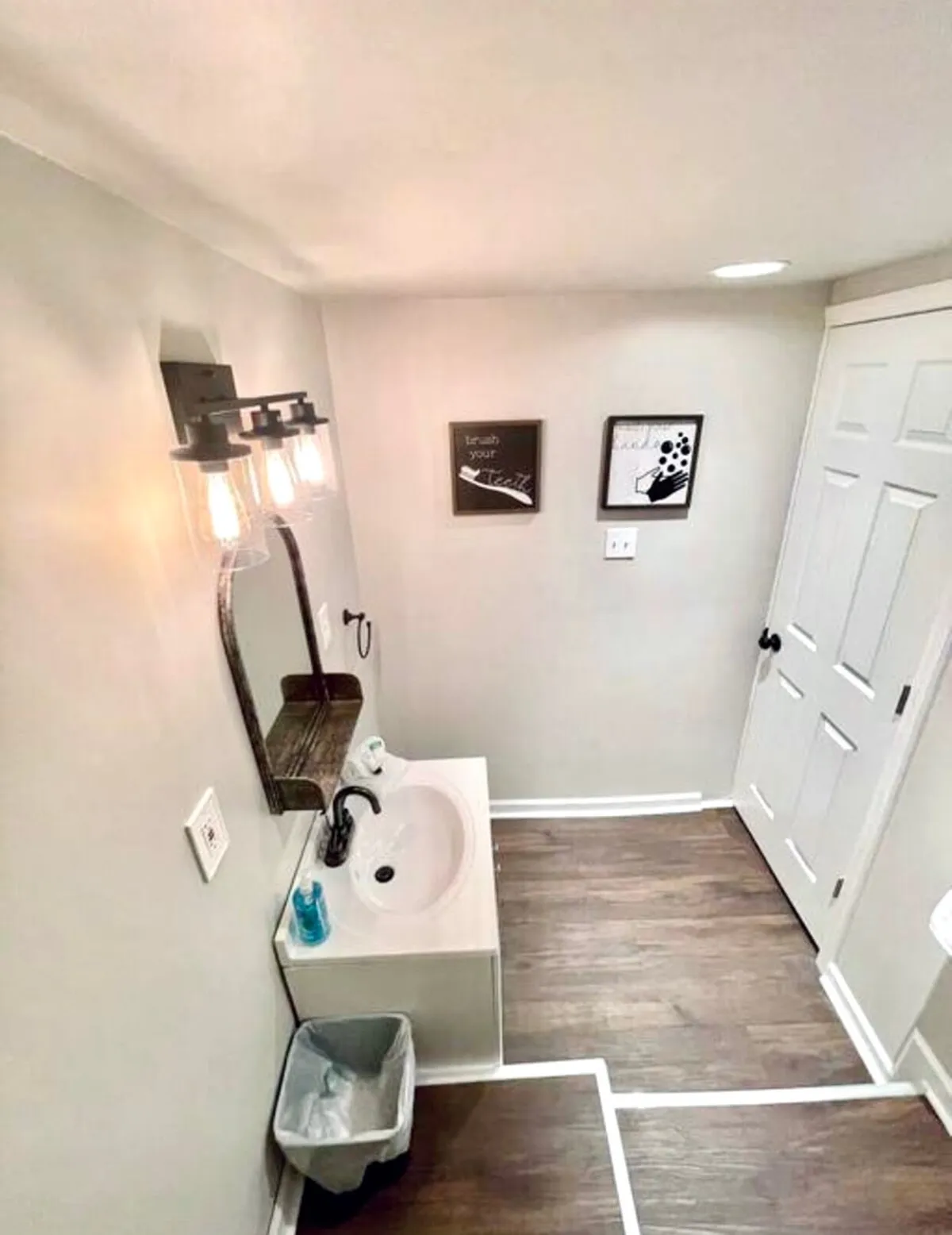 This image features a contemporary bathroom sink and mirror area adorned with a stylish light fixture and tasteful wall art. The composition is open and uncluttered, clearly illustrating essential fixtures and a functional, inviting layout.