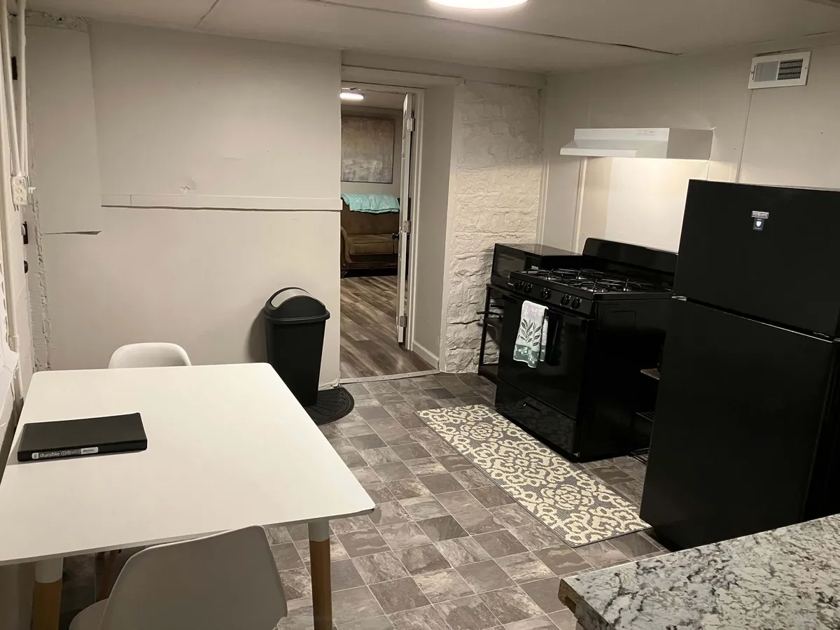 This image captures a casual and inviting kitchen and dining area with modern appliances, a well-laid dining table, and a distinct flooring pattern. The space is designed for preparing meals, enjoying quick breakfasts, or winding down after a busy day. The overall ambiance emphasizes functionality and comfort.