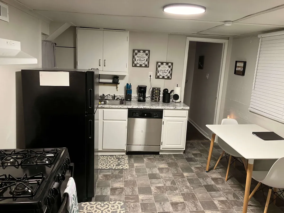 This image features a compact yet fully equipped kitchenette with a black refrigerator, stainless steel dishwasher, white cabinetry, and a kitchen table. The space is organized and inviting, with everything within easy reach for convenient meal prep or casual dining.