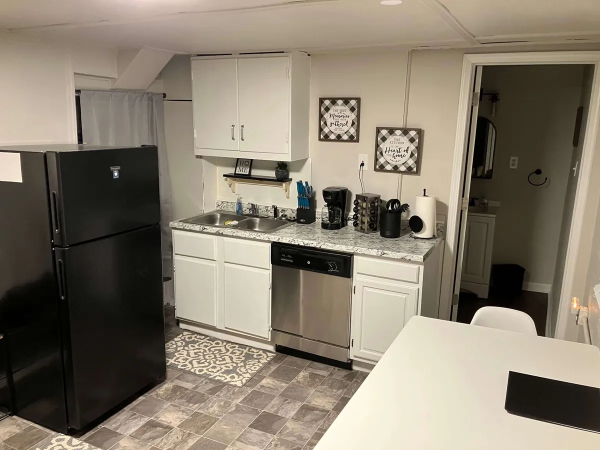 A cozy, functional kitchen scene featuring a sleek black refrigerator, granite countertops, and carefully chosen decorative wall art. The area is bathed in natural light, suggesting a welcoming spot for morning routines or quick meal prep between work or city outings.